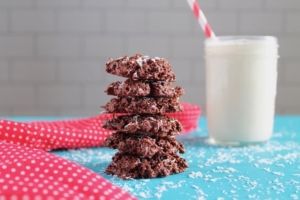 stacked coconut haystack cookies on a blue surface next to a glass of milk and a red and white polka dot napkin