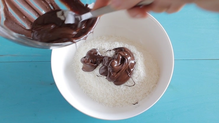 White bowl filled with white shredded coconut with melted chocolate being poured over it