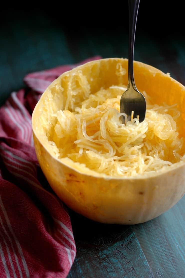 Halved spaghetti squash cooked with loosened tendrils inside and a fork