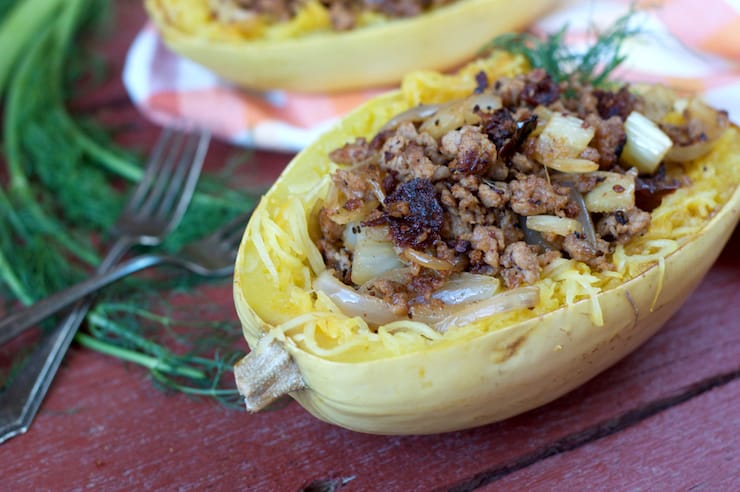 Halved cooked spaghetti squash with sausage mixture inside on wooden table