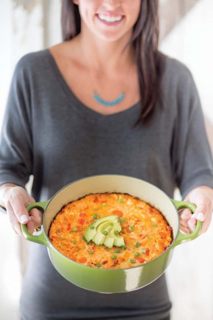 Woman holding pot with orange crusted casserole with avocado on top