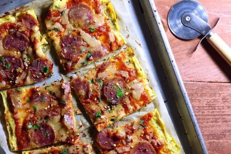 Metal baking sheet with square-cut pizza crust made from spaghetti squash topped with tomato sauce, cheese and pepperoni