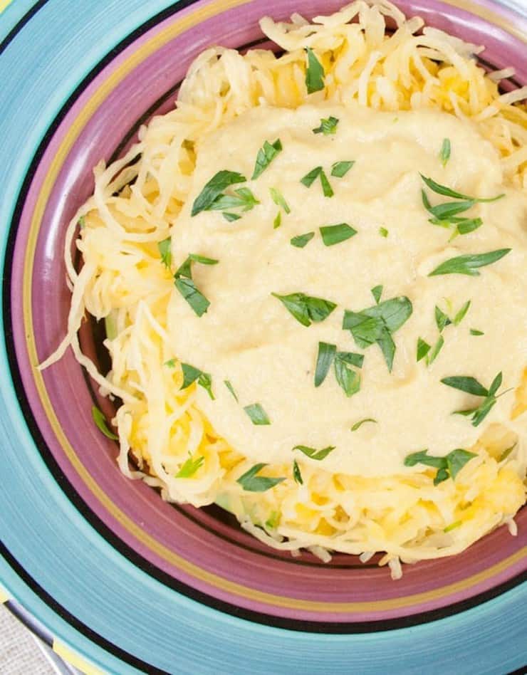 Colorful striped bowl filled with loose yellow spaghetti squash topped with cream sauce and herbs