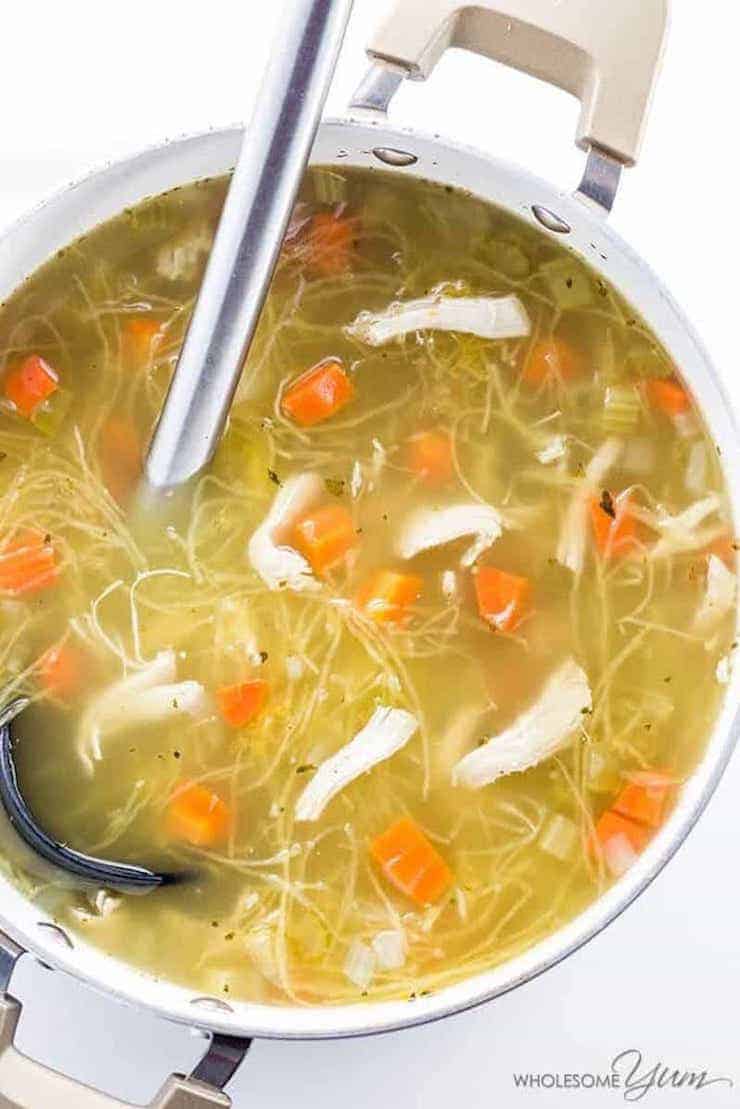 Chicken soup with spaghetti squash and carrots in a large metal pot with metal ladel