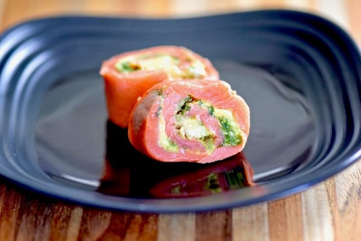 A close up of two avocado salmon pinwheels on a black plate