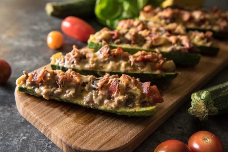 A close up of zucchini stuffed with meat on a wooden board