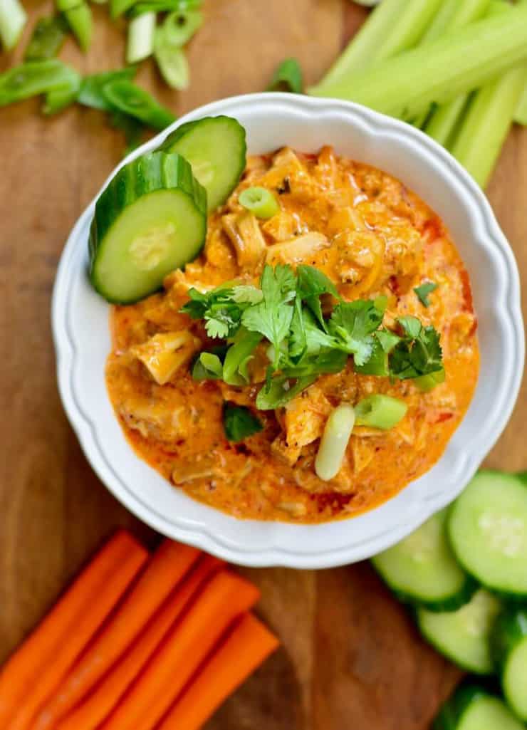 A white bowl of buffalo chicken dip topped with pickles and chopped herbs