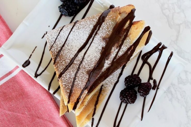 folded keto crepes sprinkled with powdered sugar and drizzled with chocolate