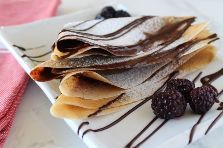 Close up side view of stacked crepes on white plate