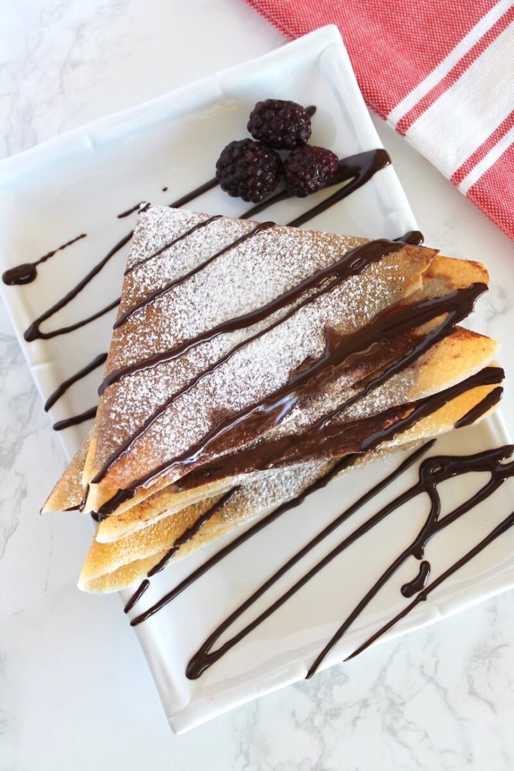 Folded stacked keto crepes with powdered sugar and drizzled melted chocolate on top
