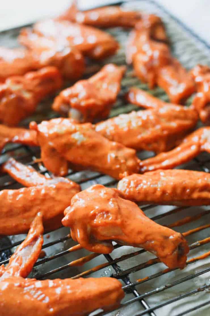 Chicken wings covered in a red sauce on a baking rack ready to be baked