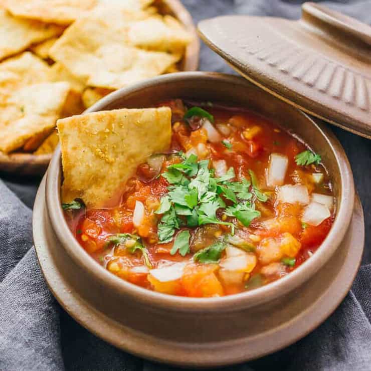 A small bowl filled with Mexican salsa and a chip dipping into it