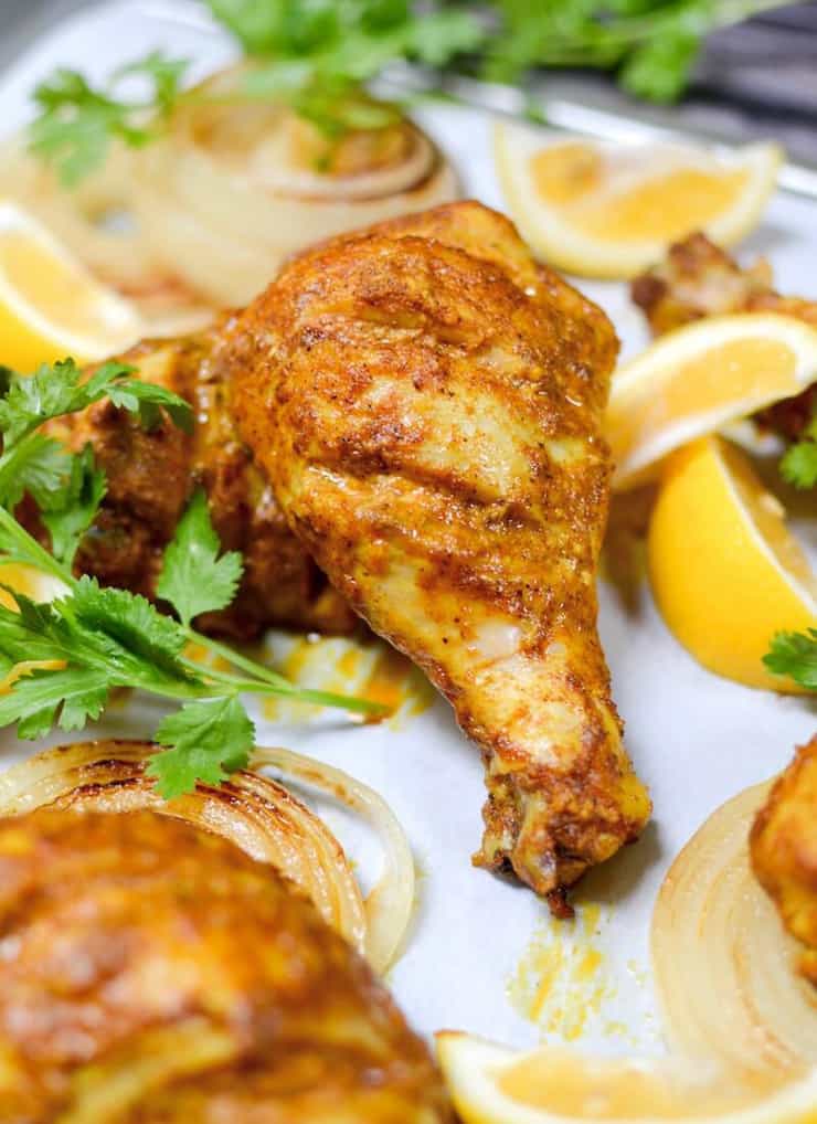 A close up of tandoori chicken on a plate with lemon wedges