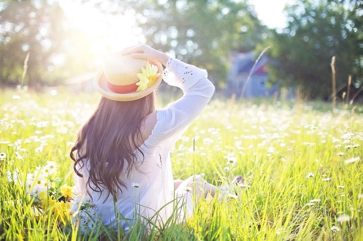 Woman with a hat on sitting in green field