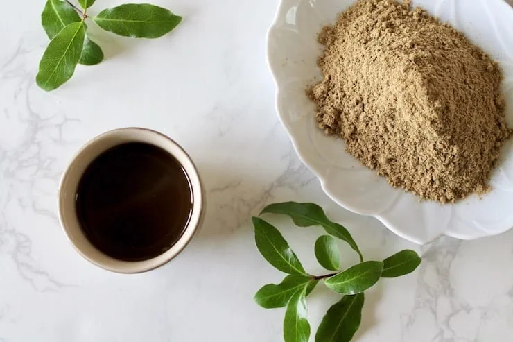 Overhead view of cup of essiac tea with powder and leaves beside it