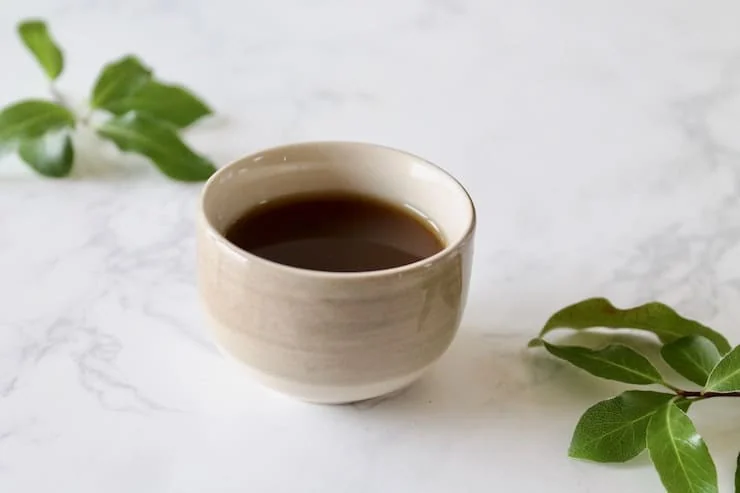 Close up of cup of essiac tea with green leaves beside it