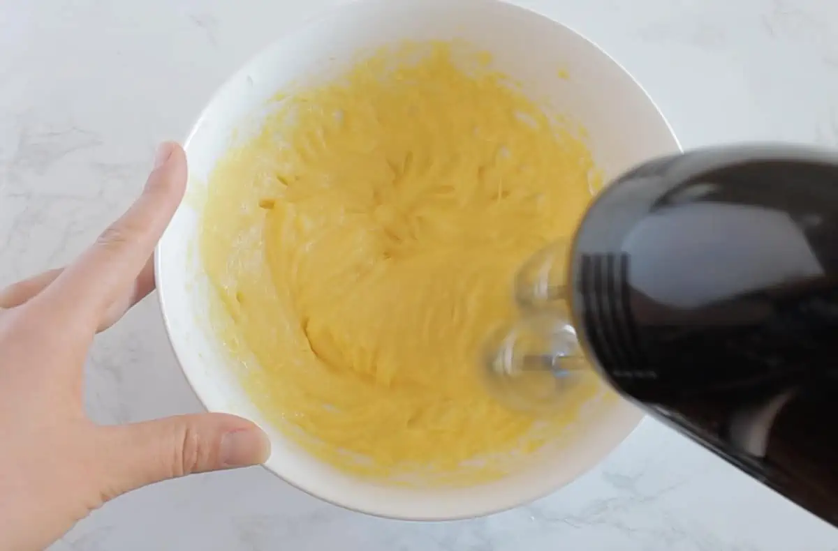 Yellow egg yolk and coconut oil mixture in white bowl being blended with electric mixer