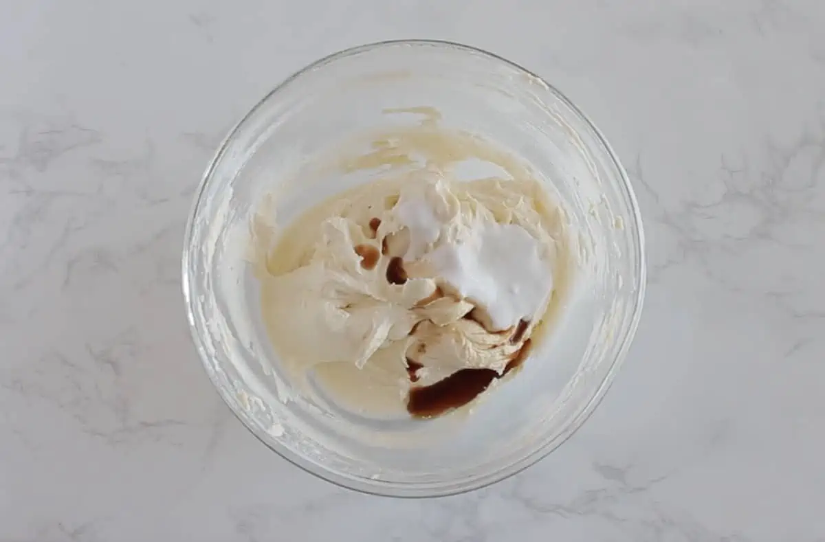 Keto buttercream frosting in clear bowl with vanilla extract and coconut cream added in the clear bowl