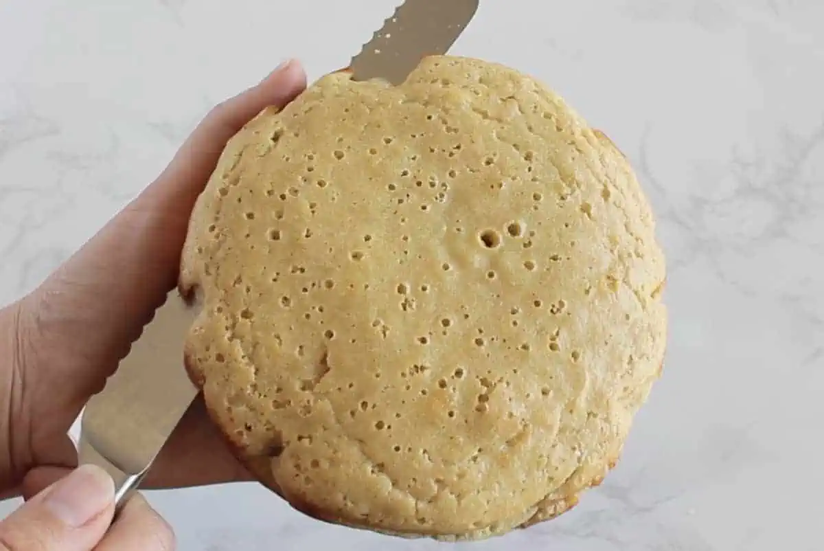 Baked coconut flour cake being cut in half with a knife