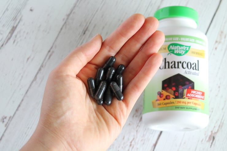 Hand holding black capsules with activated charcoal bottle in background