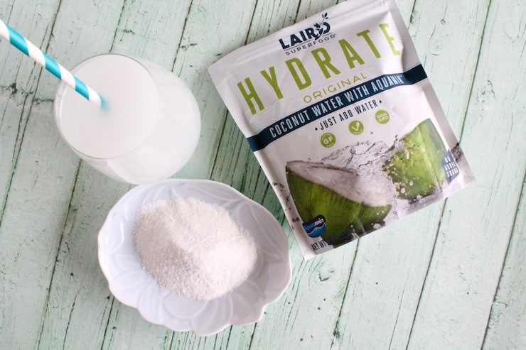 Package of Coconut water powder next to a plate with powder on it next to a glass of coconut water