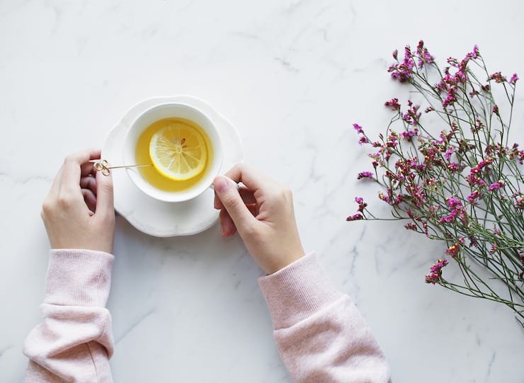 Overhead view of tea in white tea cup with saucer with womans hands holding it