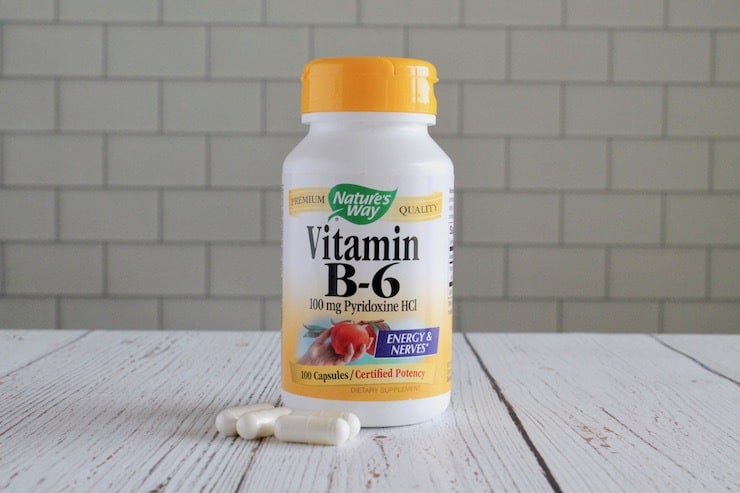 Bottle of vitamin b6 with white capsules next to it on white wooden table
