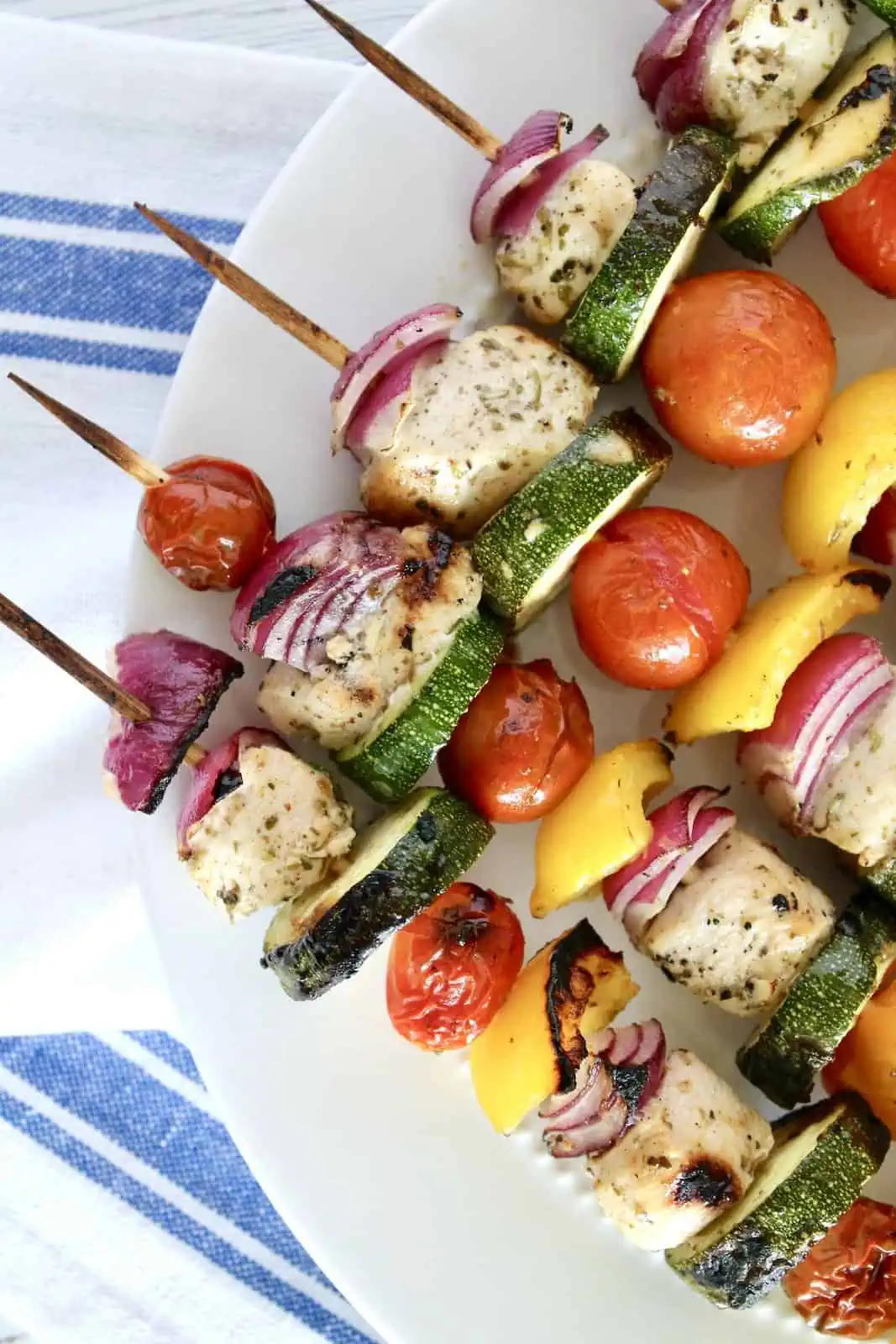 Close up of vegetable and chicken kabobs on wooden skewers on white plate