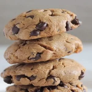 close up of four keto chocolate chip cookies stacked on a white plate with white background