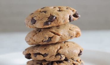 close up of four keto chocolate chip cookies stacked on a white plate with white background