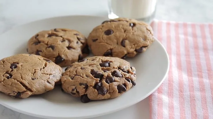 Close up of four keto cookies next to each other on a white plate with a glass of milk next to it on a pink striped towel