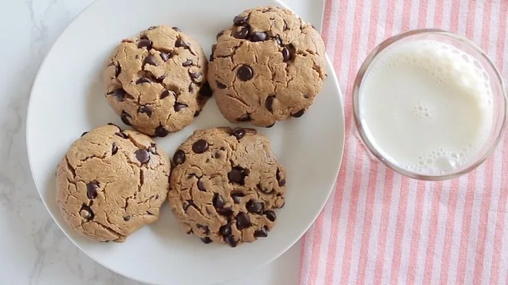 four keto cookies next to each other on a white plate with a glass of milk next to it on a pink striped towel