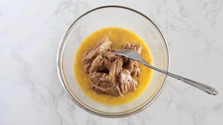 Clear bowl of dough mixture with yellow beaten eggs and cashew butter mixing