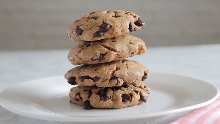 four keto chocolate chip cookies stacked on a white plate with white background
