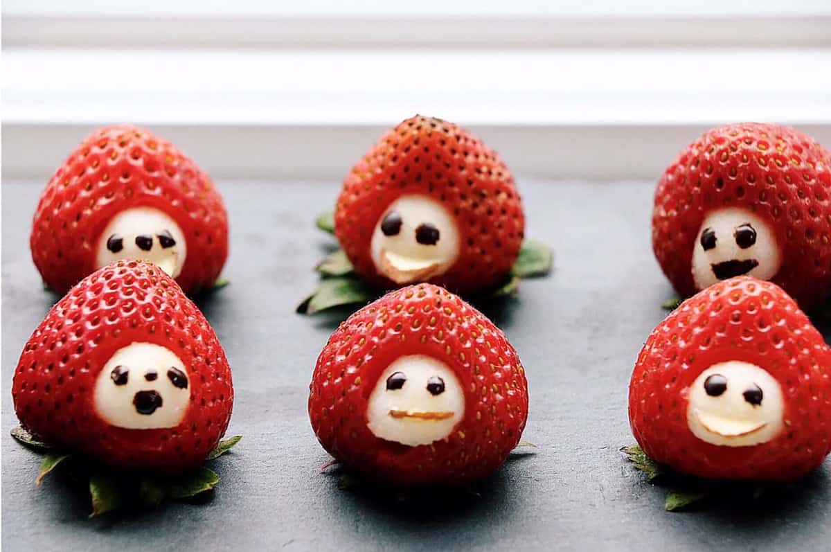 six strawberries in a row with white spots on them with faces drawn on them