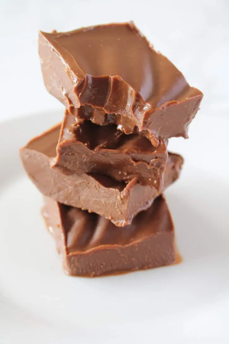 four pieces of chocolate keto fudge stack on top of each other on a white plate with a bite taken out of the top piece