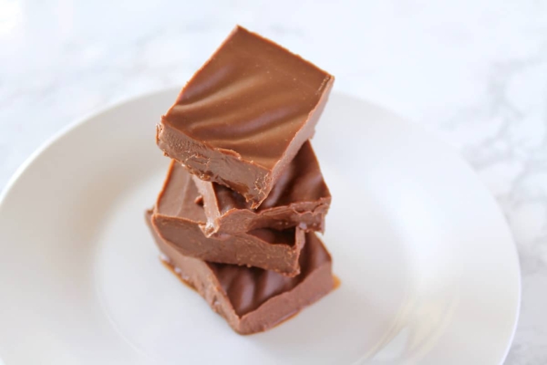 four pieces of chocolate keto fudge stack on top of each other on a white plate