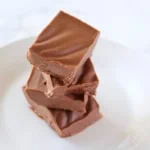 four pieces of chocolate keto fudge stack on top of each other on a white plate