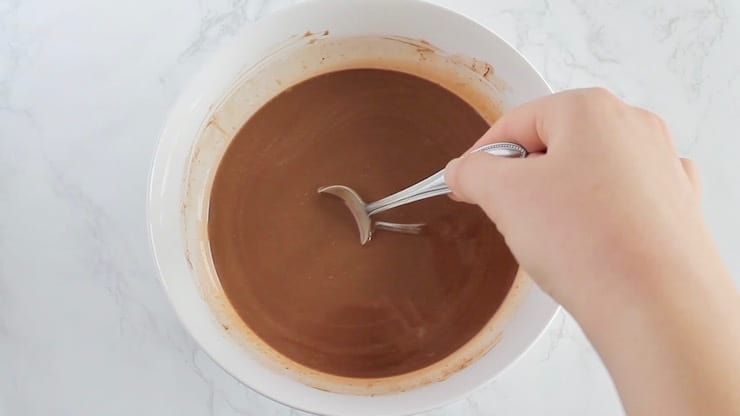 Keto fudge ingredients melted together in a white bowl with a hand stirring it with a spoon