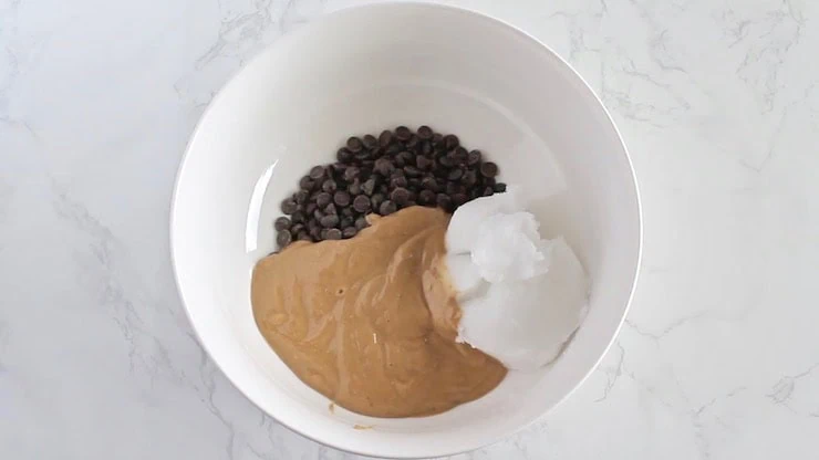 Keto fudge ingredients including chocolate chips, cashew butter and coconut oil in a white bowl