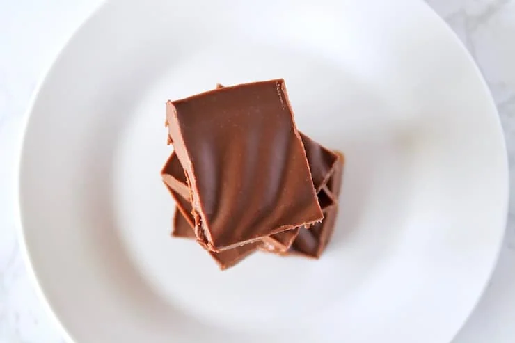 Overhead view of four pieces of chocolate keto fudge stack on top of each other on a white plate