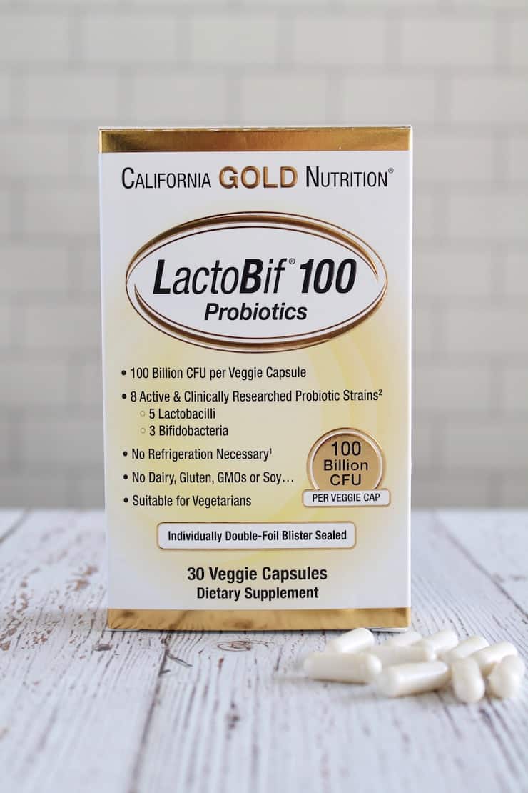 White and yellow box of probiotics on a white wooden table with white capsules next to it