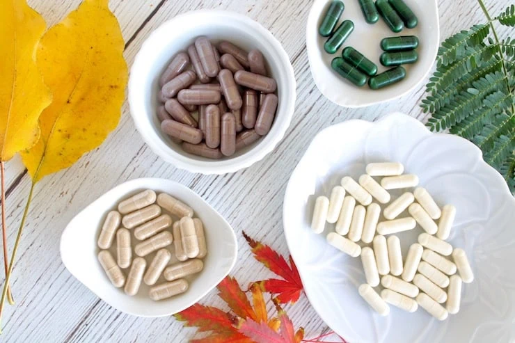 Overhead view of different colored supplement capsules in white trays with colorful plants around it