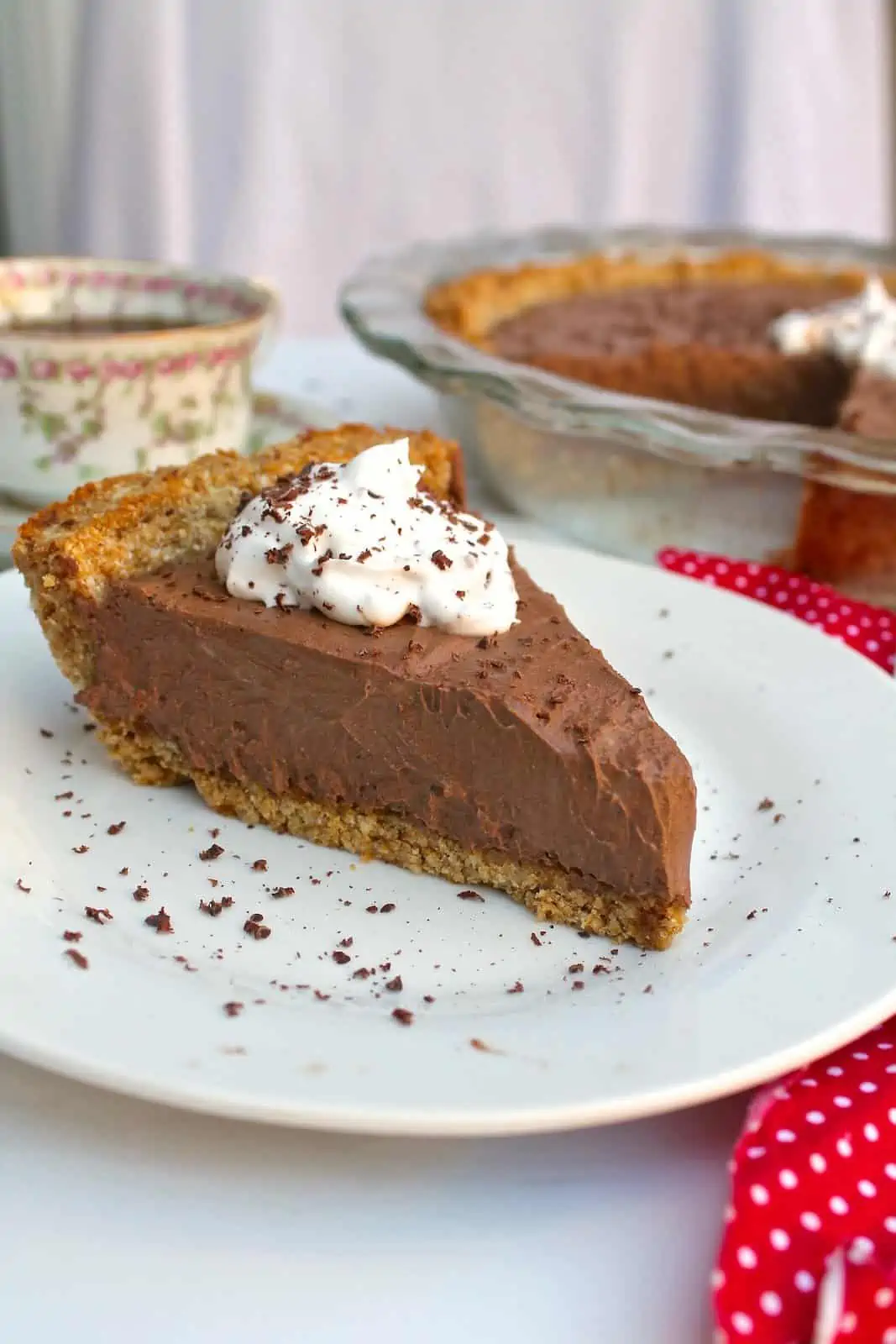 One slice of chocolate cream pie on a white plate with a dollop of white whipped cream and chocolate shavings on top