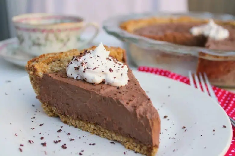 One slice of chocolate cream pie on a white plate with a dollop of white whipped cream and chocolate shavings on top