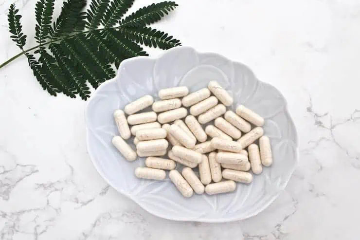 Light blue dish with white capsules in it on a white marble table next to green leaves