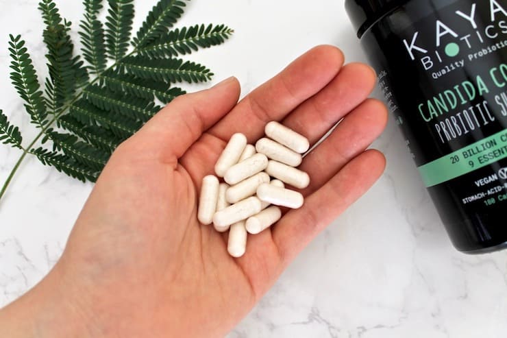 A hand holding white capsules next to a black bottle and green leaves