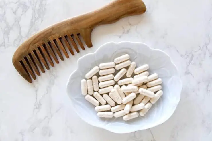 Light blue dish with white capsules in it on a white marble surface next to a wooden comb