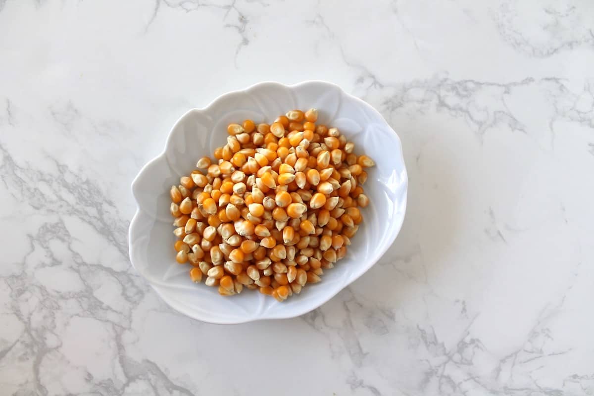 Small white dish with popcorn kernels in it on a white marble surface