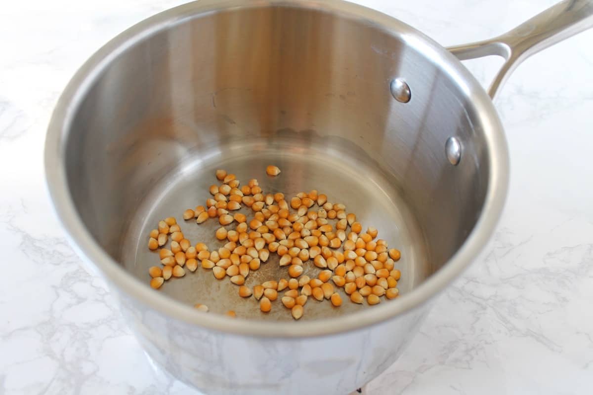 Stainless steel pot with popcorn kernels in it on a white marble surface